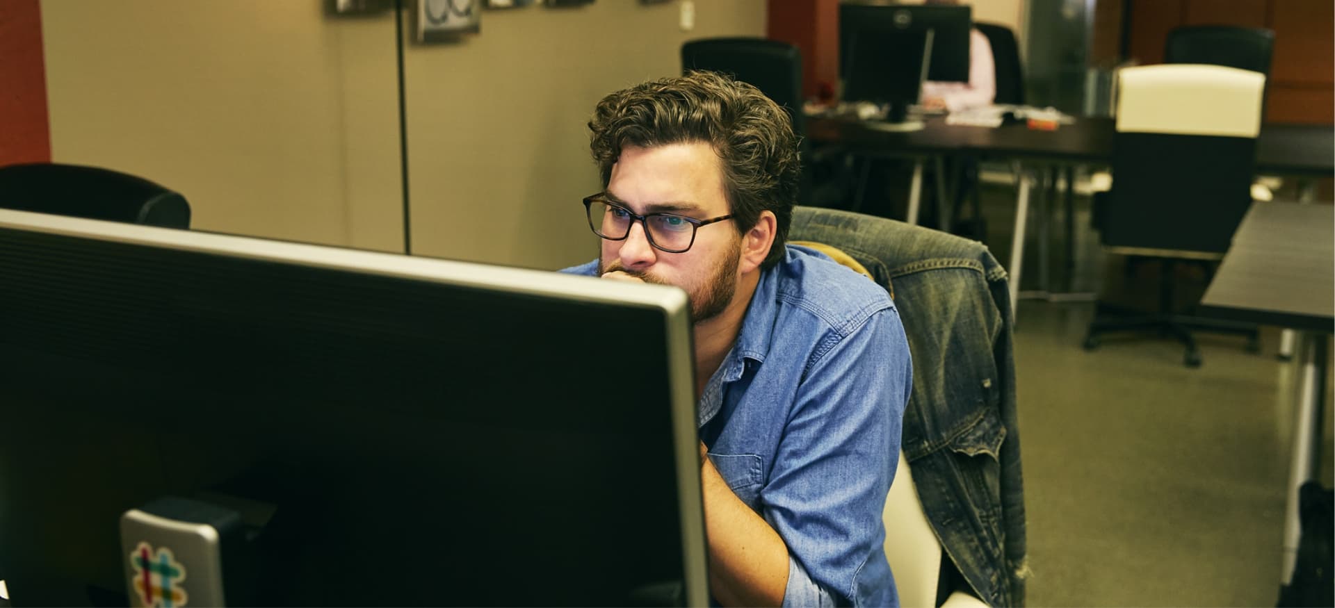 Man leans toward computer screen in coworking space.