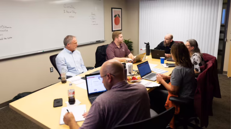 Conference table filled with people, laptops and paper
