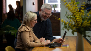 Man standing over women's shoulder while she is seated in front of a laptop computer.