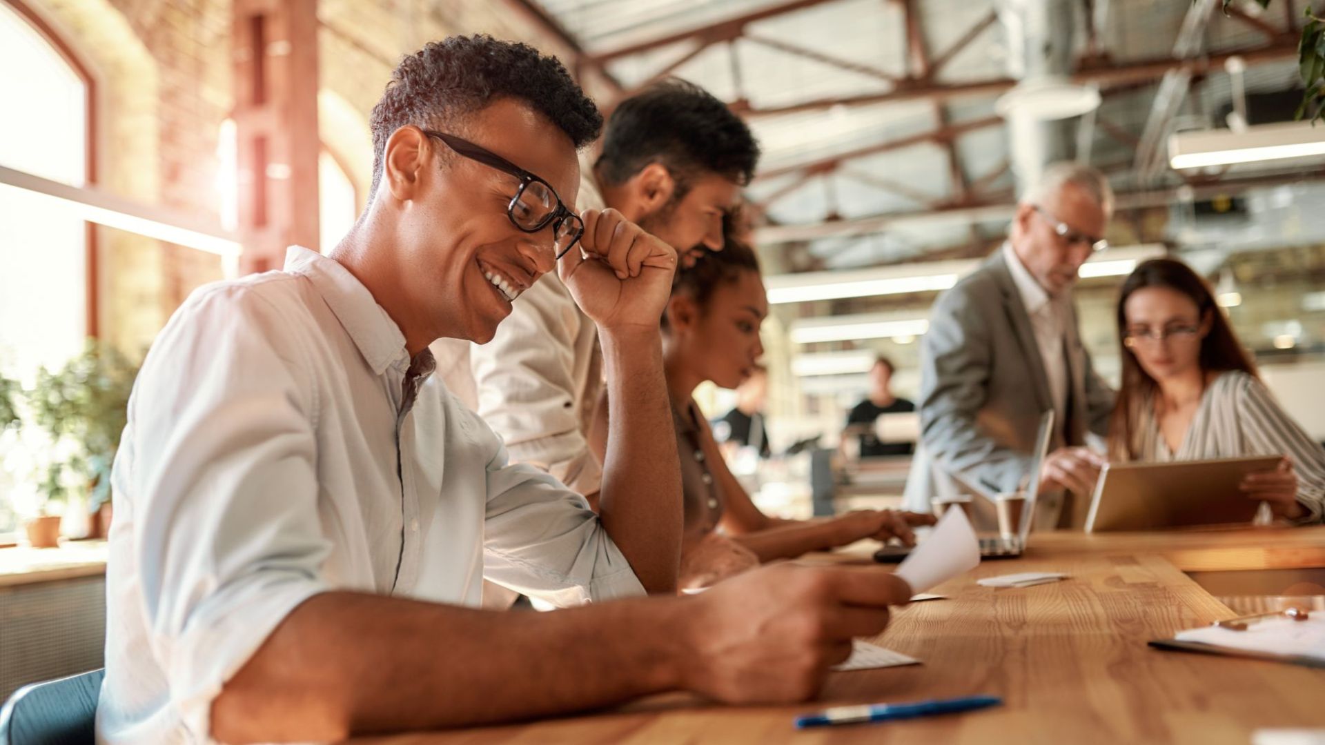 African American man in glasses smiling and seated at a conference table with a group of work colleagues.