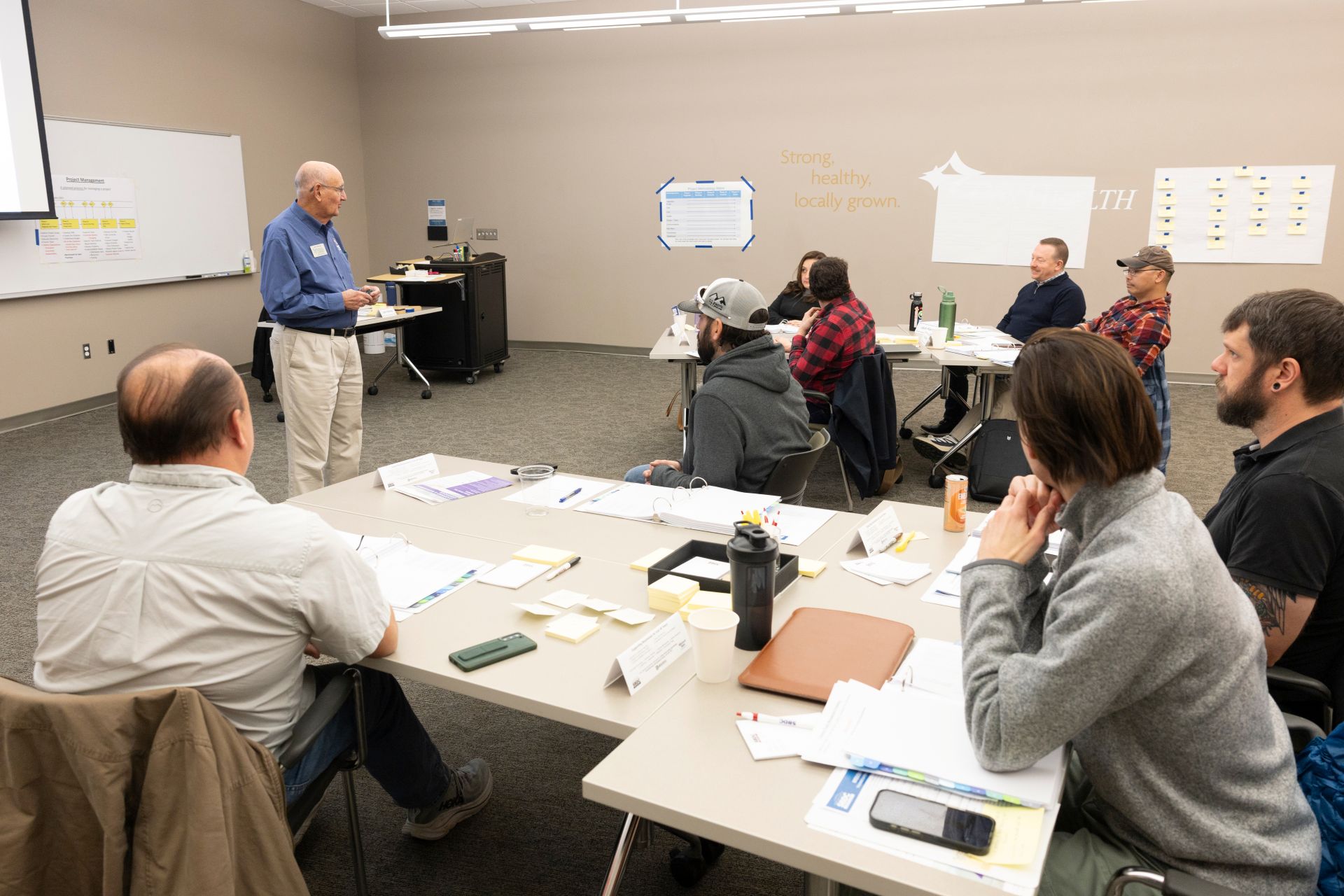 Instructor standing at the front of a classroom of project management students lecturing.