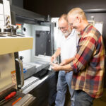 Male Supervisor showing male employee how to operate machinery in a manufacturing setting.