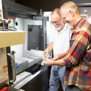 Male Supervisor showing male employee how to operate machinery in a manufacturing setting.