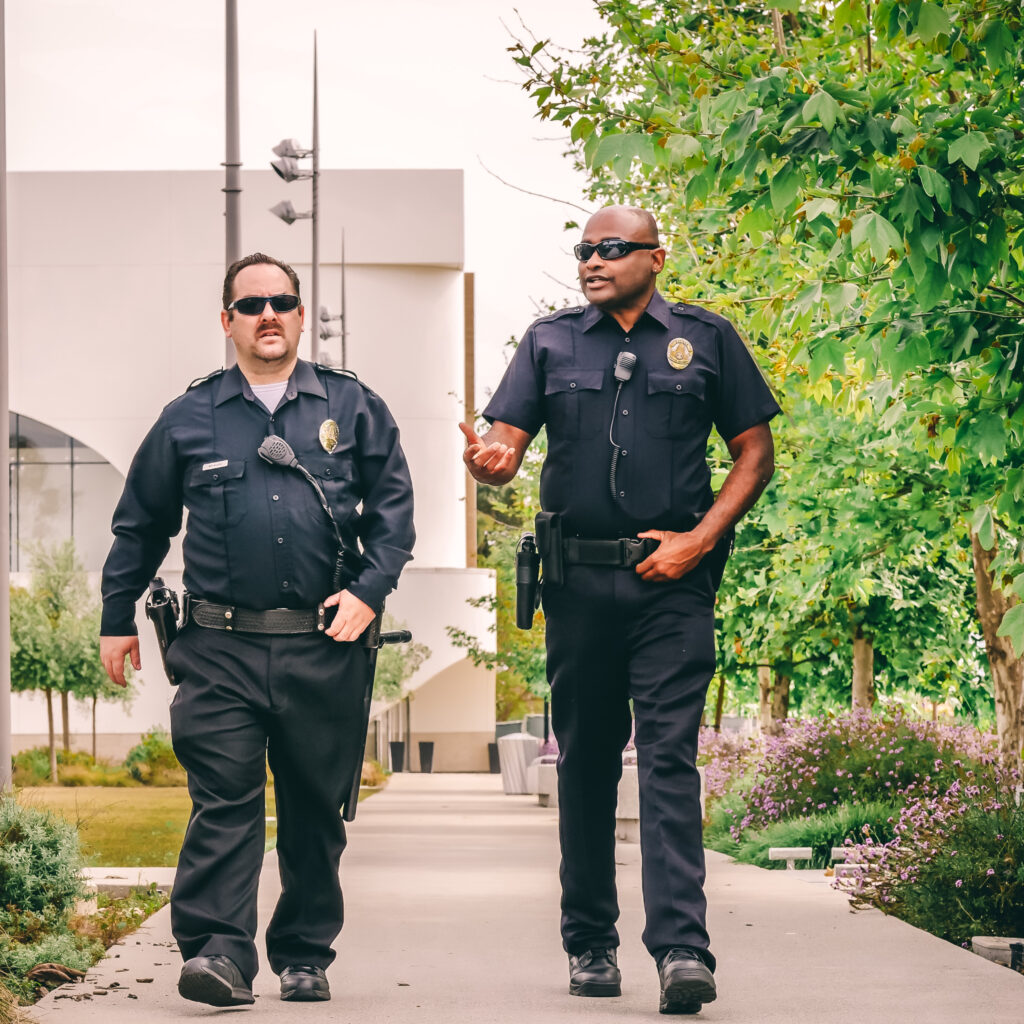 Two public safety officers walk along sidewalk.