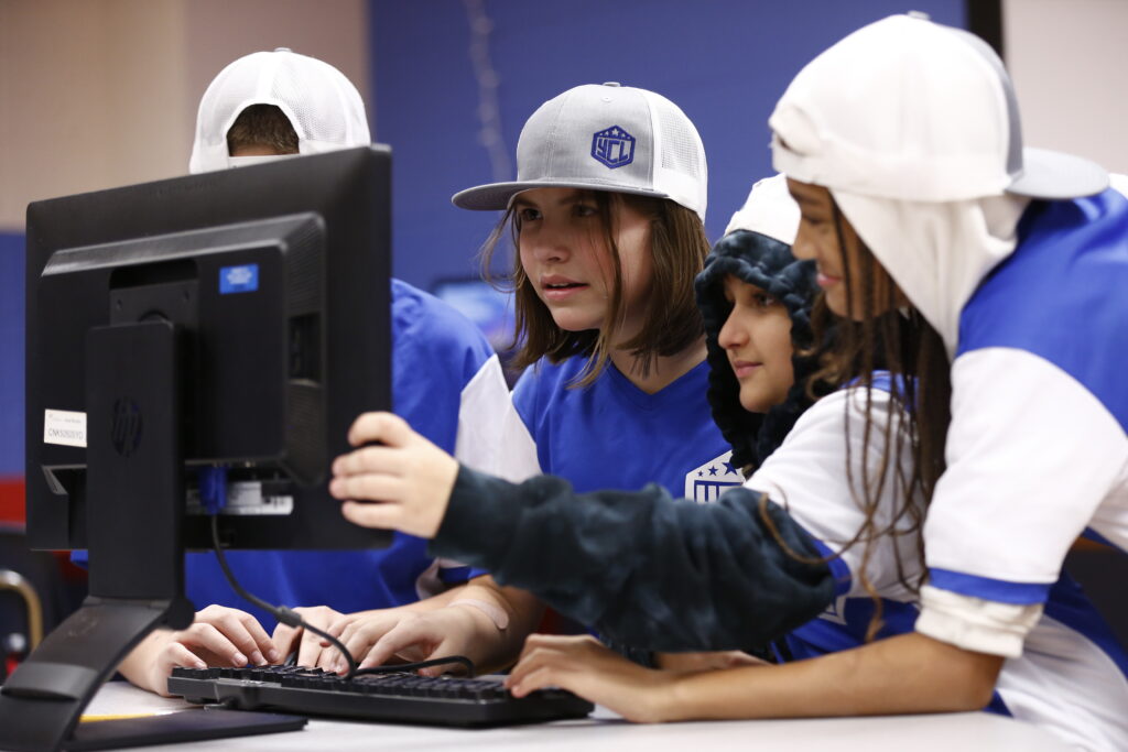 Group of Youth Code League team members gather around computer.