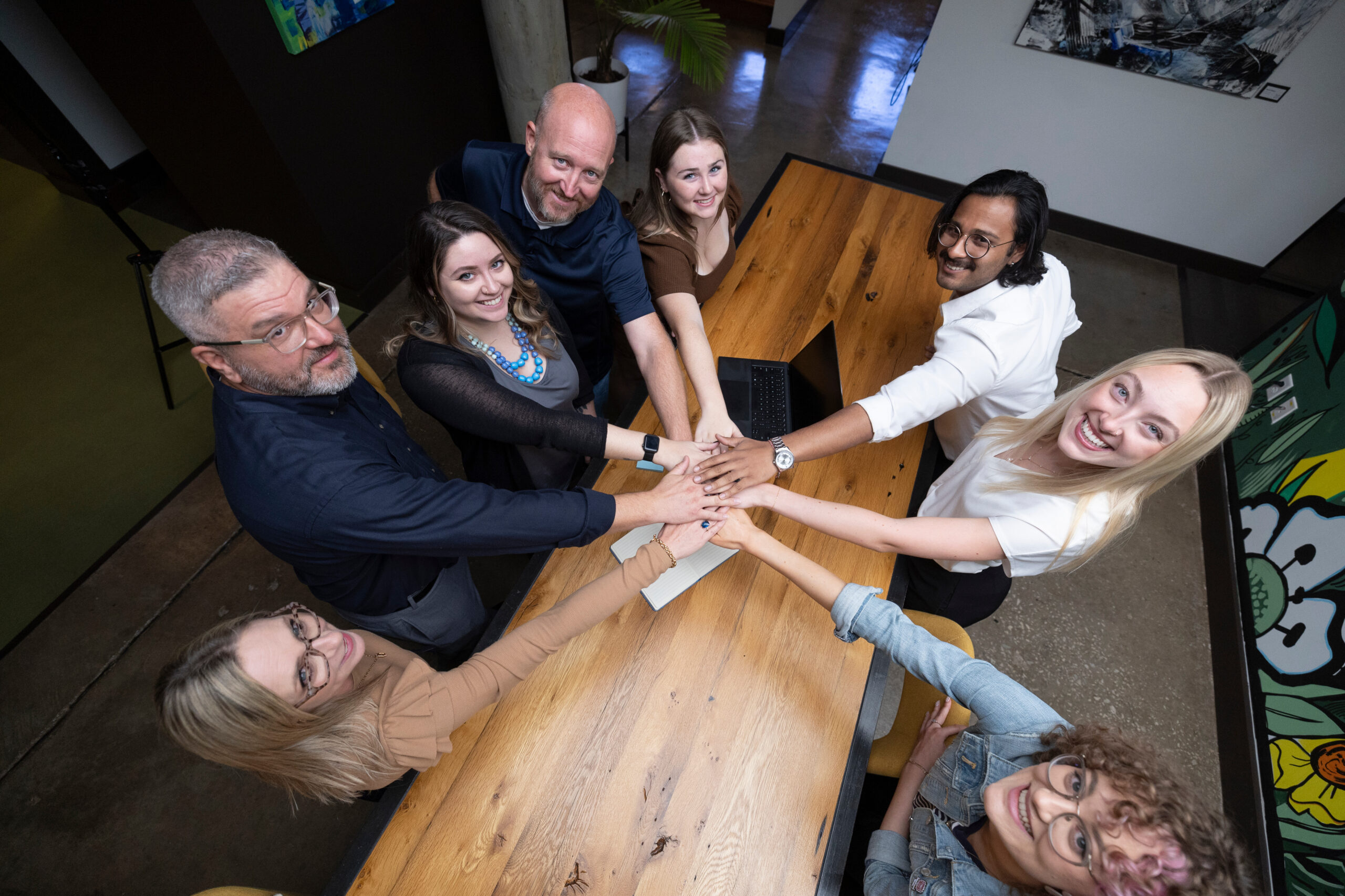 Group of business professionals gathered around a conference table putting their hands in a circle, stacked on top of each other as a team.