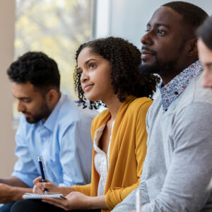 A group of business people sit in a row in a training class. They look at an unseen speaker as they concentrate on his lecture.