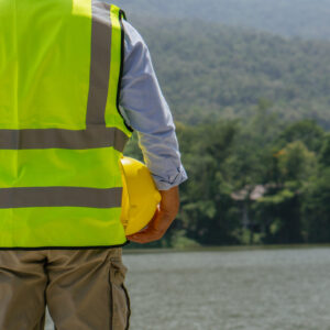 Back of engineer in neon yellow vest as he stands in front of body of water.