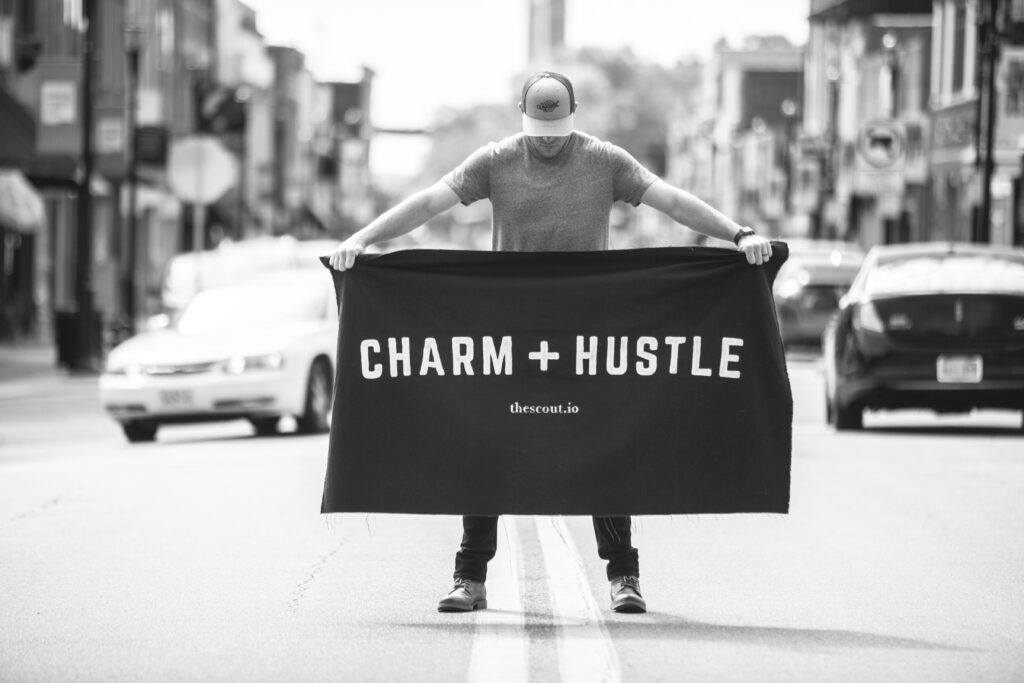 Jeff Rawson stands in mid-street with Charm and Hustle banner.