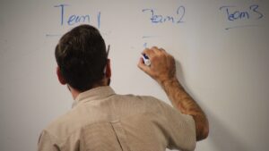 Man writes team names on whiteboard.