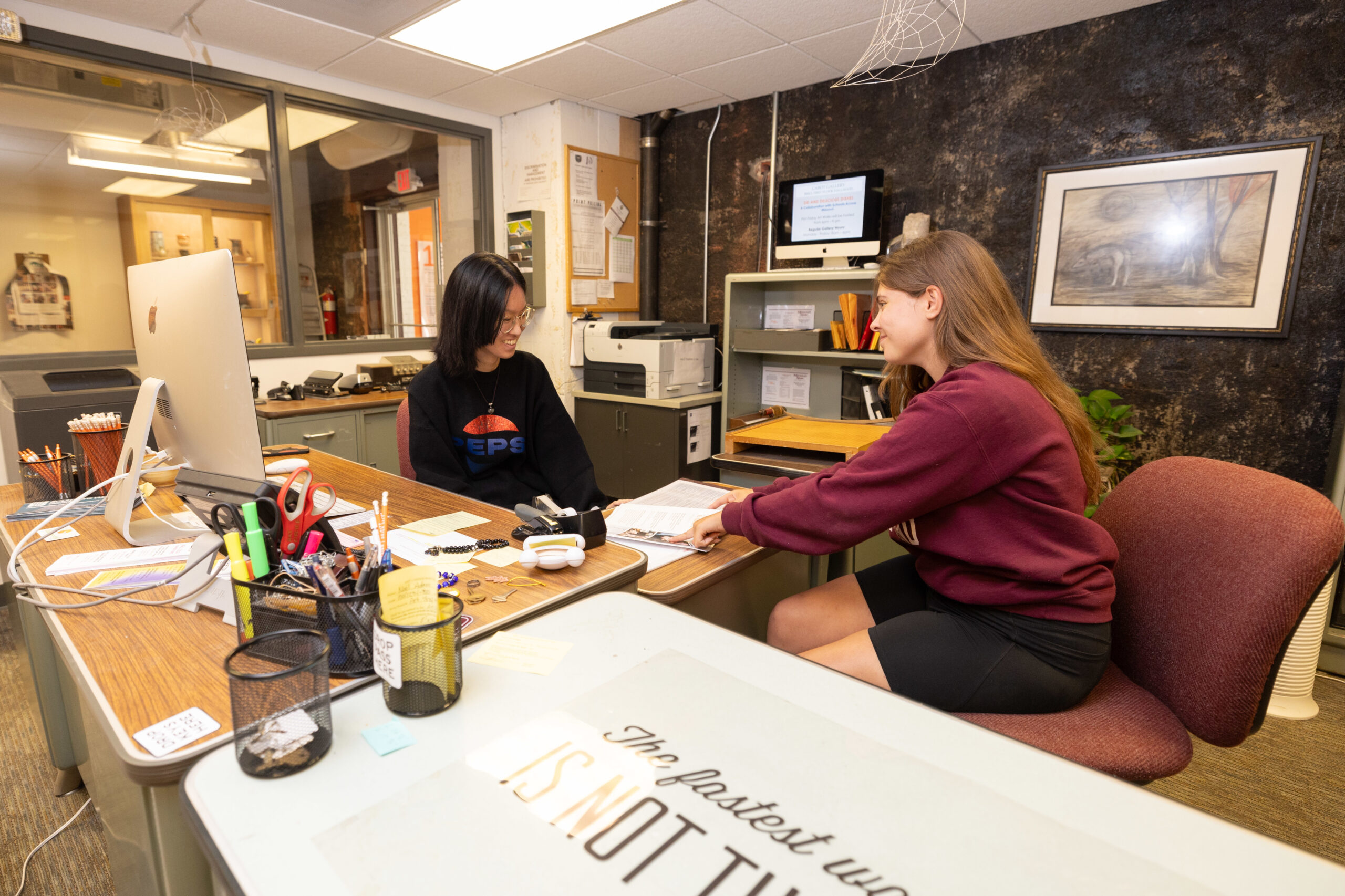 Two female student employees sit at desk in Art and Design department.