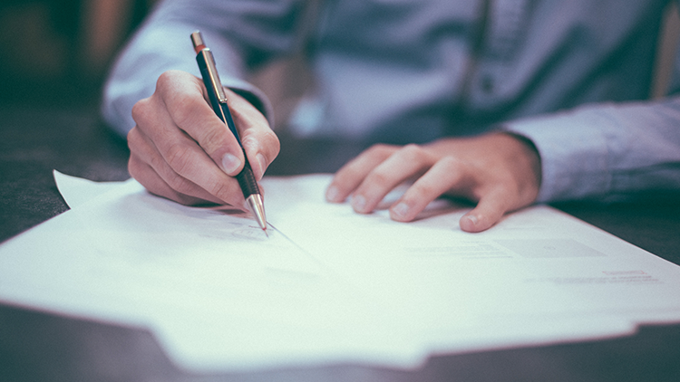 Close-up of man's hands holding a pen and writing on some paper documents.