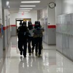 officer moving down hallway in tactical gear with guns drawn