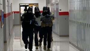 officer moving down hallway in tactical gear with guns drawn