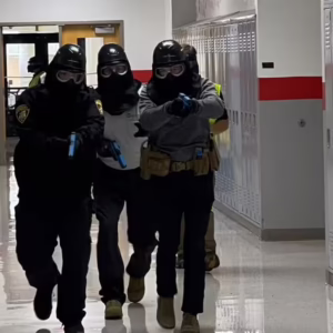 officer moving down hallway in tactical gear with guns drawn
