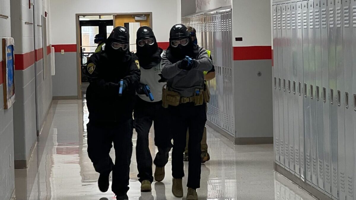 officer moving down hallway in tactical gear with guns drawn