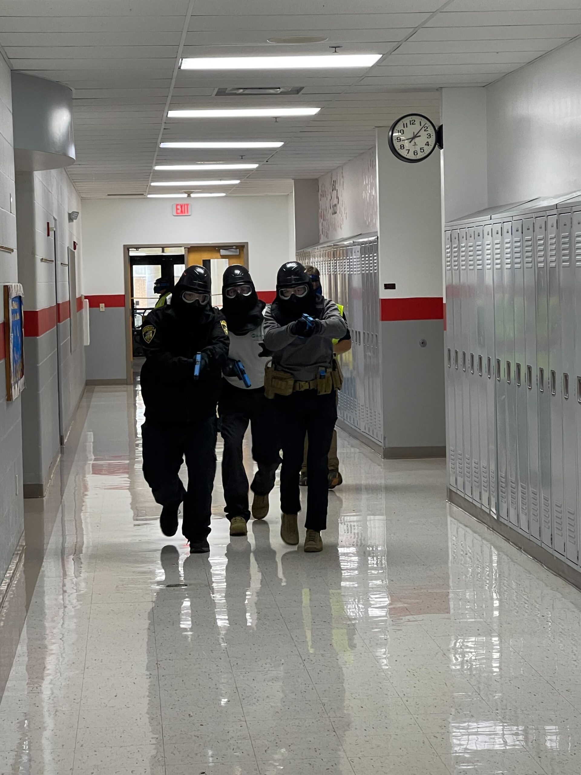 officer moving down hallway in tactical gear with guns drawn