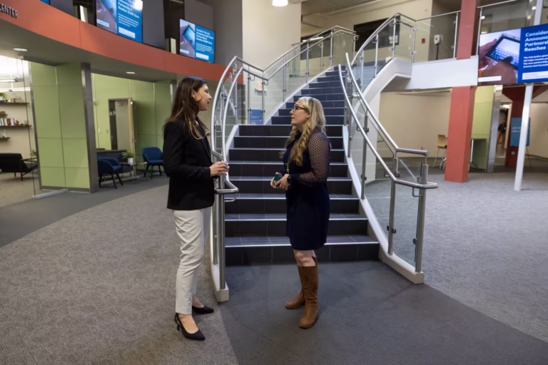 Two women talk in front of staircase