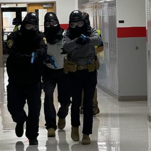 Officer running down hall guns drawn with protective gear on