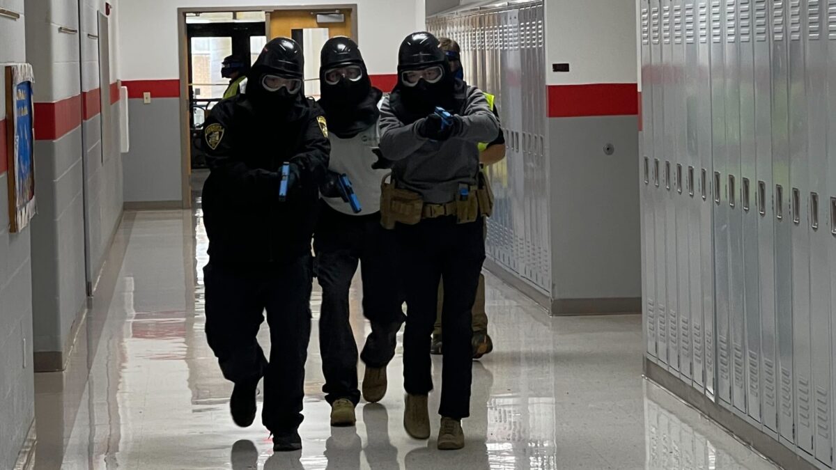 Officer running down hall guns drawn with protective gear on