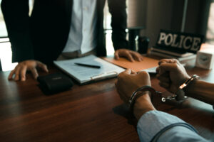 Police officer standing over desk intervewing handcuffed suspect