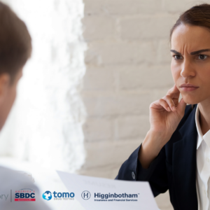 Business woman looking suspiciously at a man sitting across the table from her. The man's back is facing the camera and he is slightly blurred in the image.