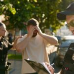 two police officers calming upset man in tan shirt