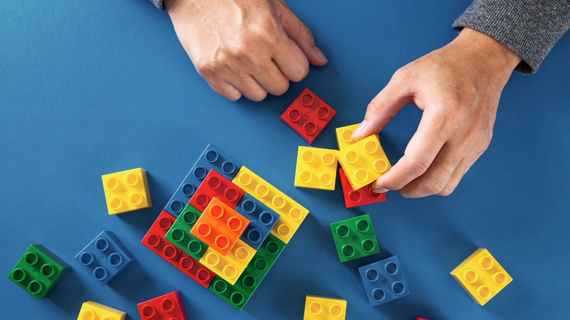Hands placing LEGOs on blue background