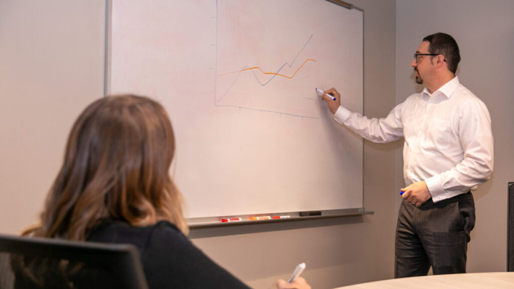 Man draws on white board while woman takes notes