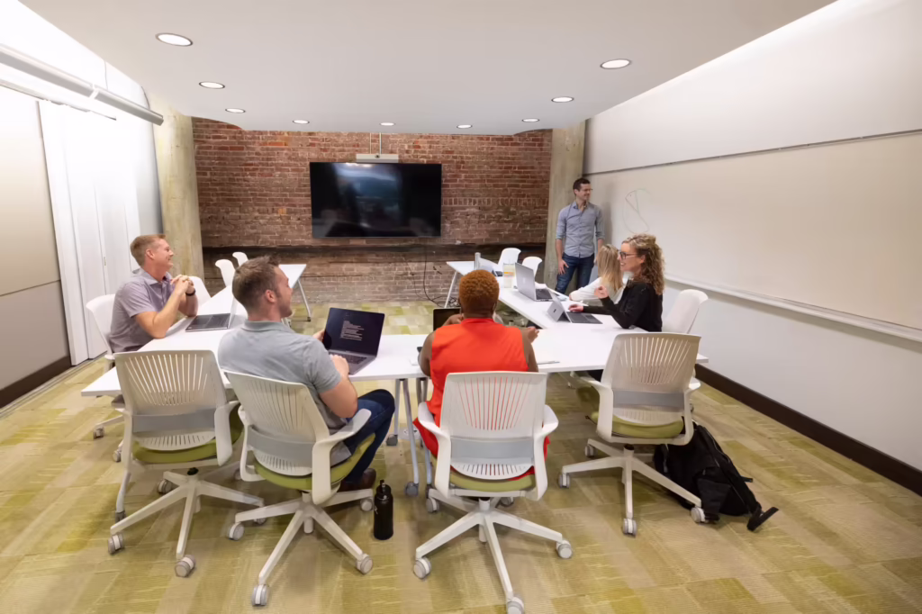 Group gathered in conference room. One man draws on whiteboard