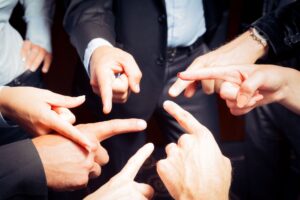 Hands of seven business men and women pointing at each other.