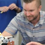 Man sitting behind a LEGO scene with an airplane and LEGO mini-figure.
