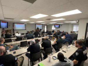 room full of law enforcement officers with screens and tvs turned on for a presentation with instructor standing in front