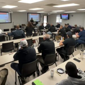 room full of law enforcement officers with screens and tvs turned on for a presentation with instructor standing in front