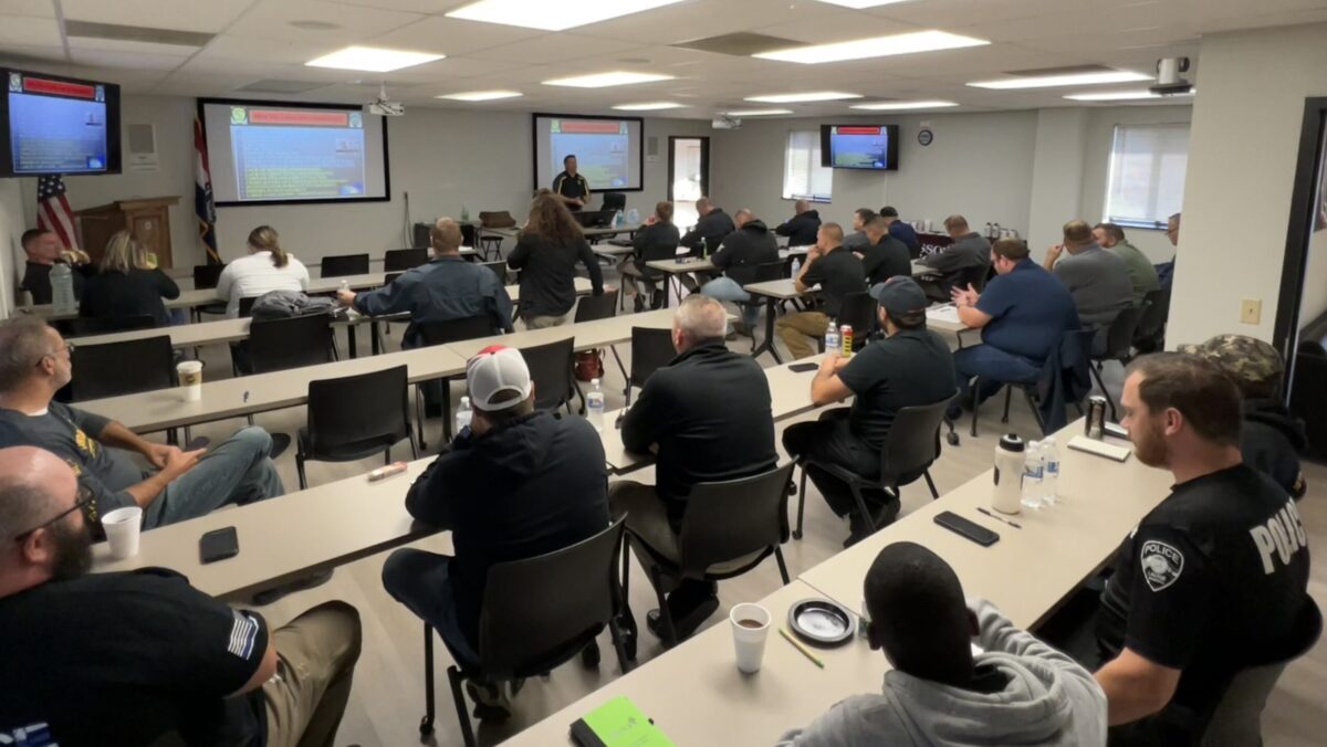 room full of law enforcement officers with screens and tvs turned on for a presentation with instructor standing in front