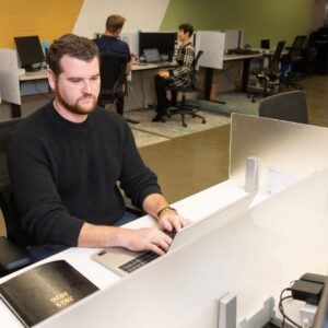 Man sitting in front of a laptop with his hands on the keyboard with a 2025-2026 planner sitting on the desk next to him.
