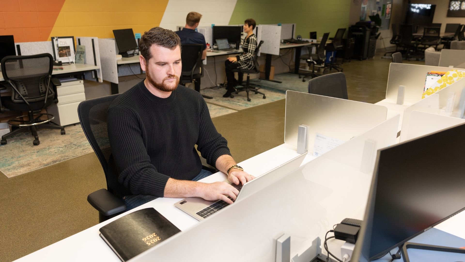 Man sitting in front of a laptop with his hands on the keyboard with a 2025-2026 planner sitting on the desk next to him.