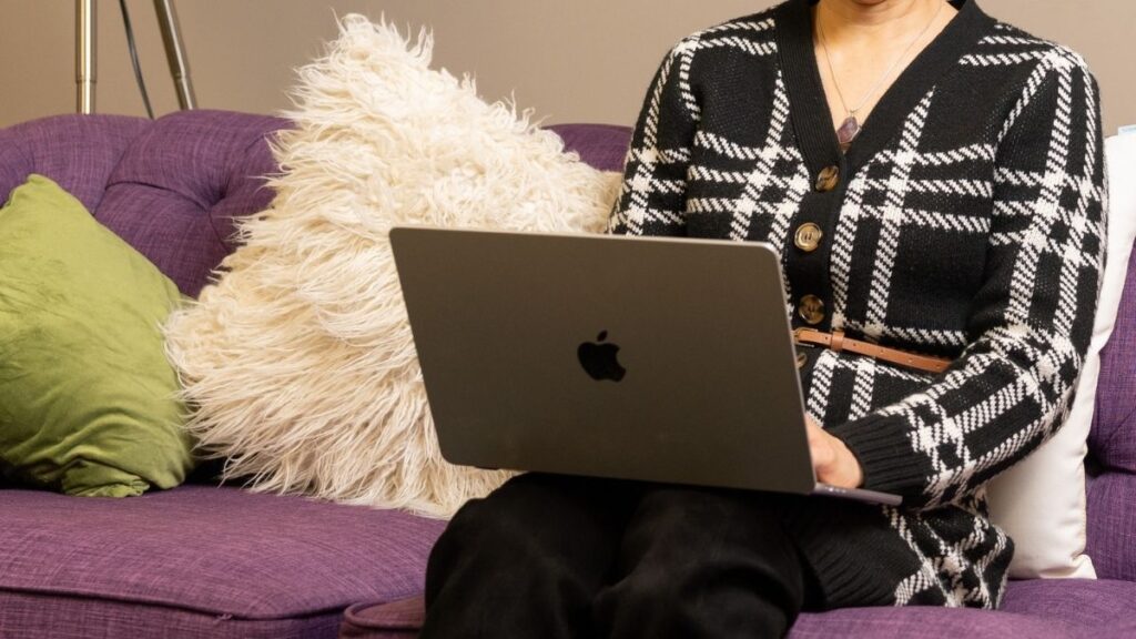 Woman sits on couch with laptop