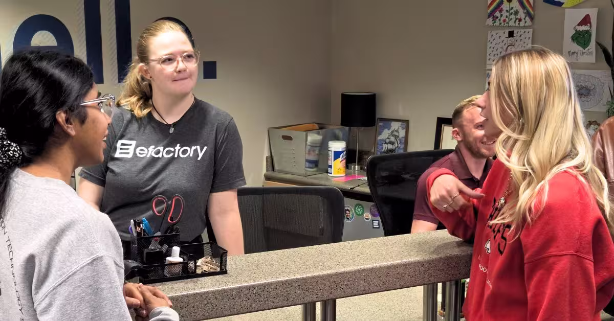 Three students stand at efactory front desk