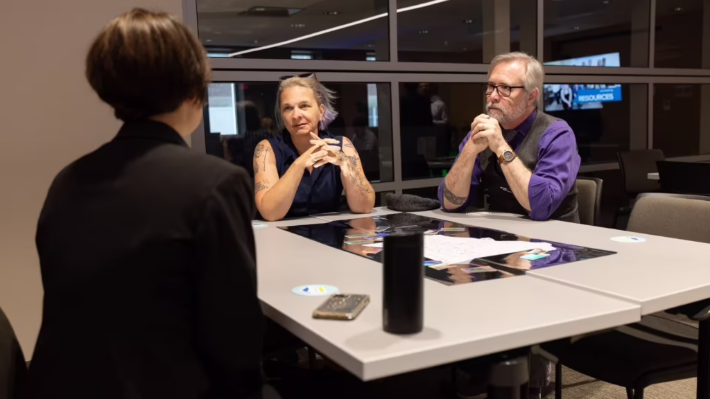 Three people sit at table talking about business