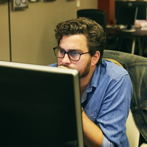 Man leans toward computer screen in coworking space.