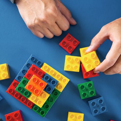 Hands placing LEGOs on blue background